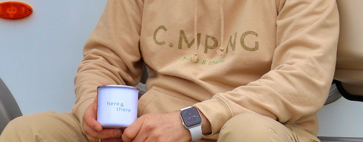 Ein Mann hat gerade Camping Geschenke von C.MP.NG erhalten und sitzt vor einem Camper
