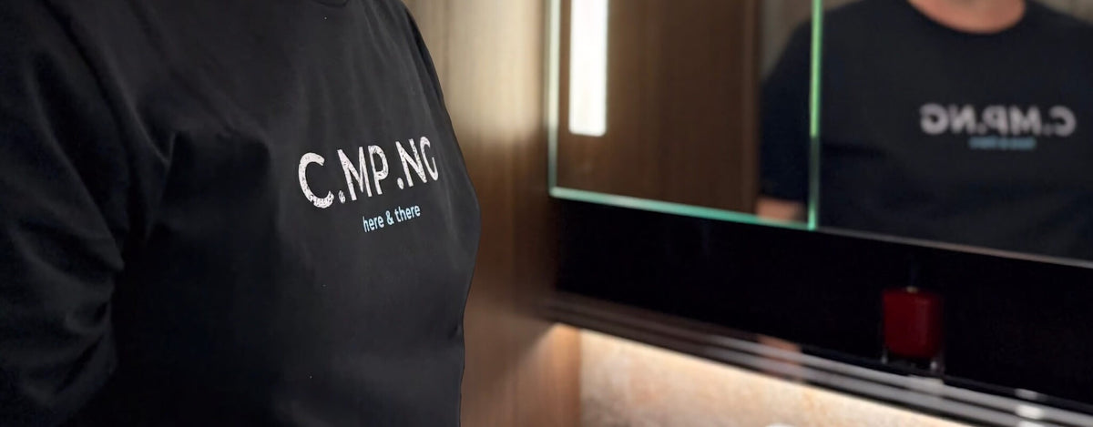 Ein Mann steht mit einem C.MP.NG Camping T-Shirt vor einem Spiegel