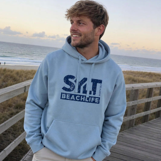 Mann in hellblauen Hoodie mit dunkelblauen 'SYLT NORTH SEA BEACHLIFE' Logo, steht auf Sylt.